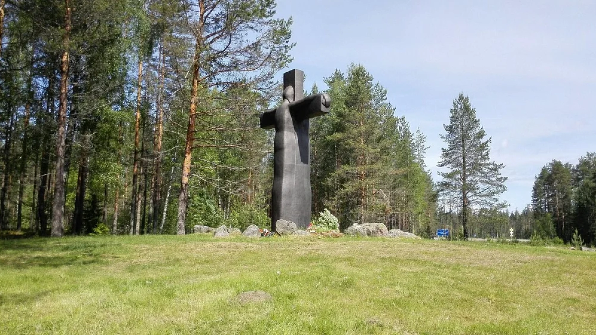 Пятиметровый чугунный Крест скорби на холме, окруженный валунами и соснами