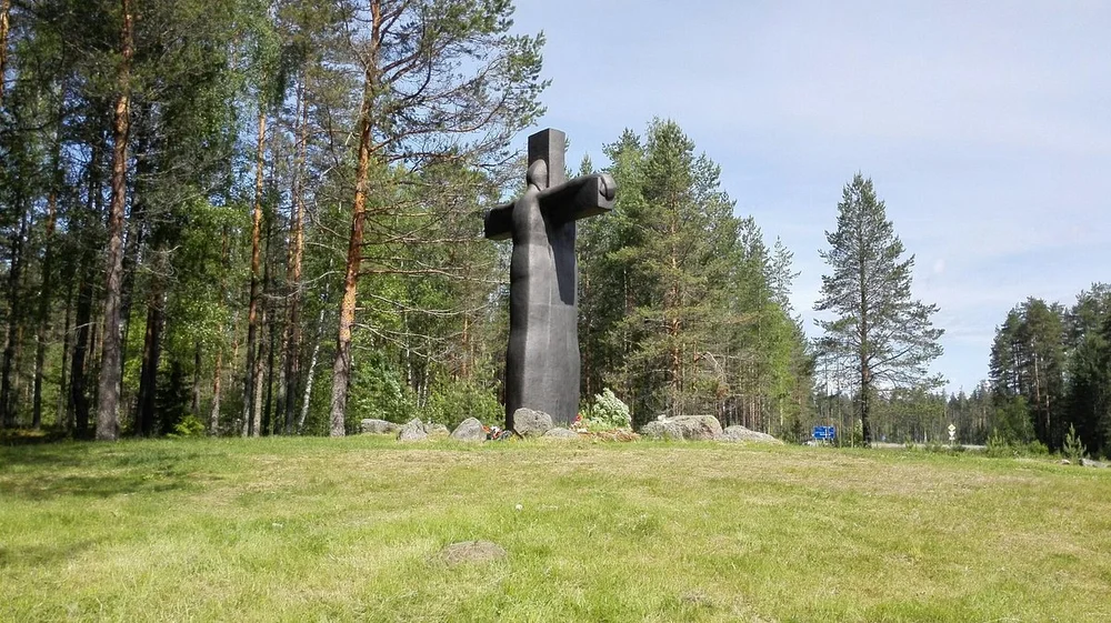 Пятиметровый чугунный Крест скорби на холме, окруженный валунами и соснами