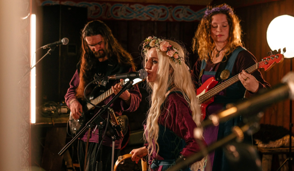 Музыканты в исторических костюмах с цветочными венками играют на электрогитарах на фестивале «Kirjálaland» — Карельская земля. Живая музыка средневековой тематики на площадке Исторического парка «Бастiонъ».